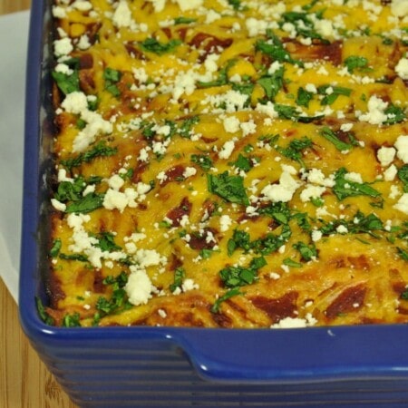 Baked casserole in a blue dish, topped with chopped herbs and crumbled cheese.