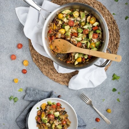 A bowl and pan of colorful vegetable quinoa salad with tomatoes, cucumbers, and herbs on a gray surface—an inviting twist on classic favorites like black bean quinoa casserole.