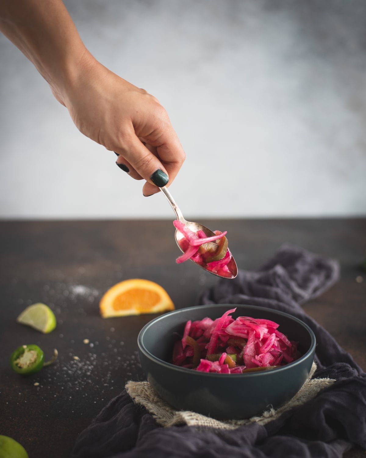 Hand with spoon scooping pickled red onions from bowl