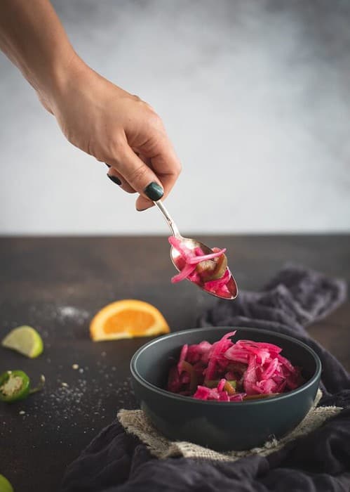 Hand with spoon scooping pickled red onions from bowl