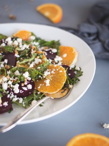 arugula salad on a white plate with beets and orange