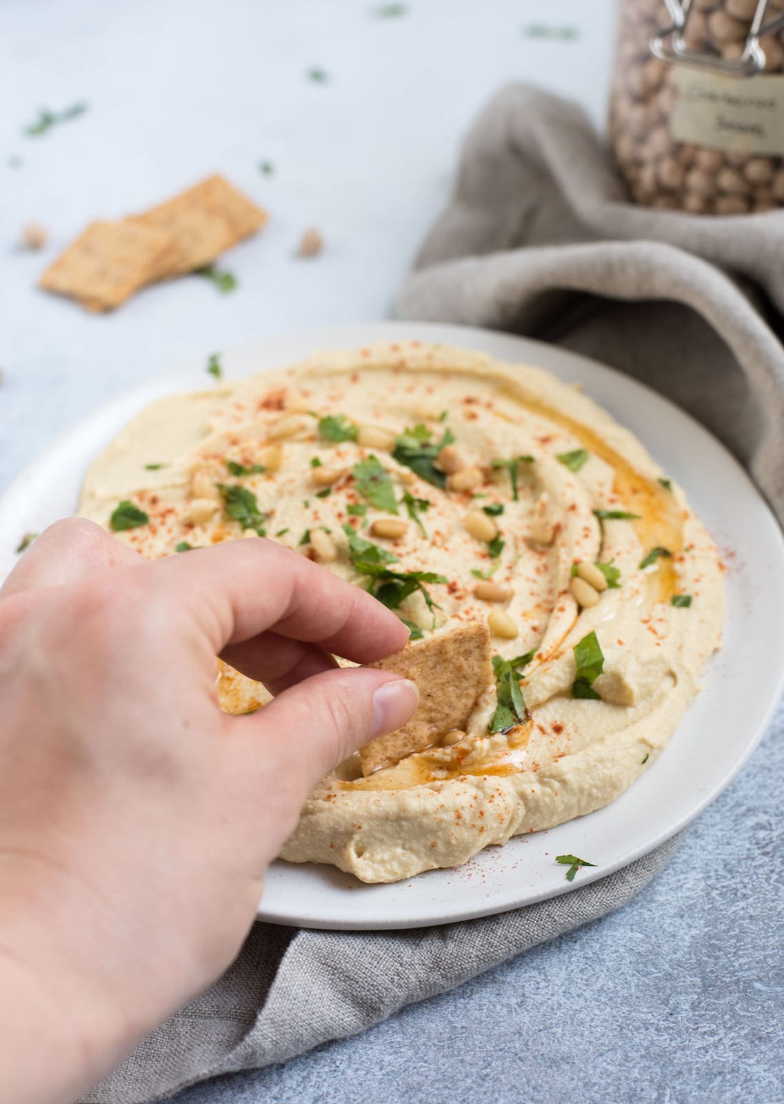 hand scooping up classic hummus onto a cracker