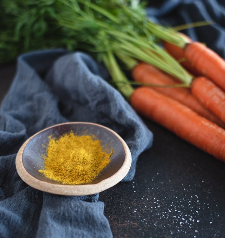 A bowl of curry powder with carrots on dark background