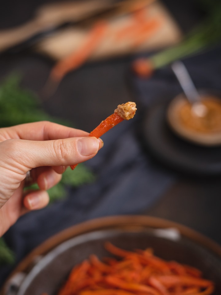 hand holding carrot fry that was dipped in sauce