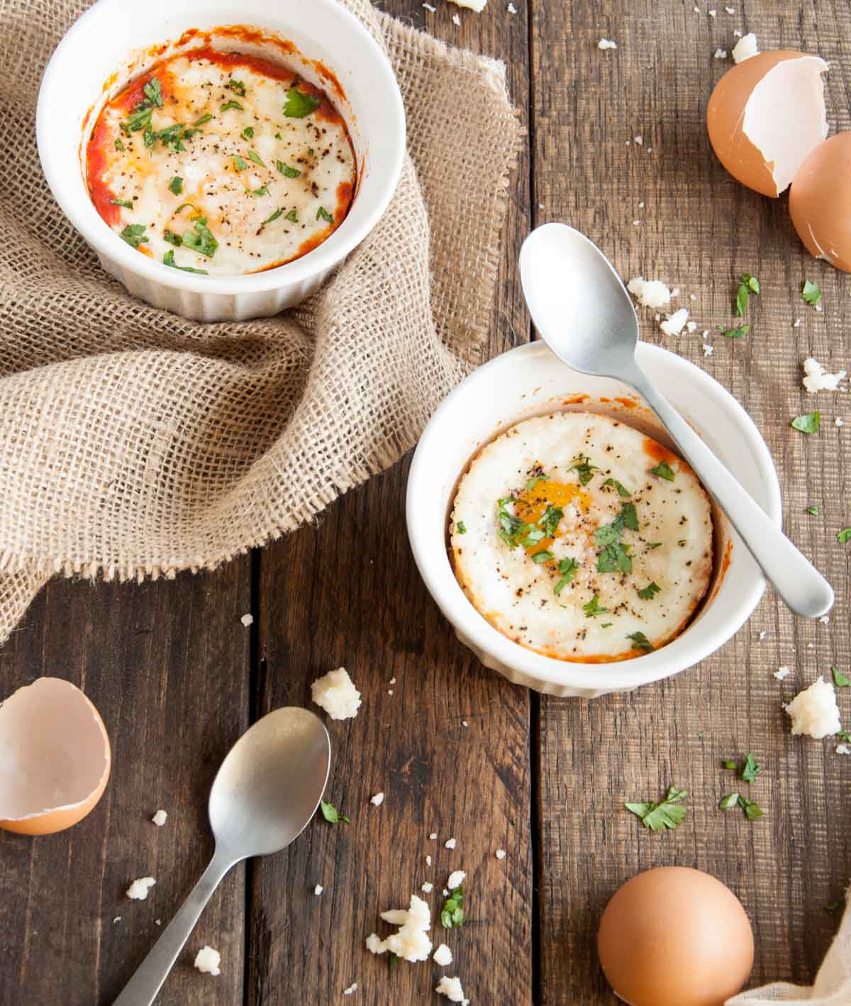 Close up of baked eggs in two small ramekins sitting on a wooden table top.