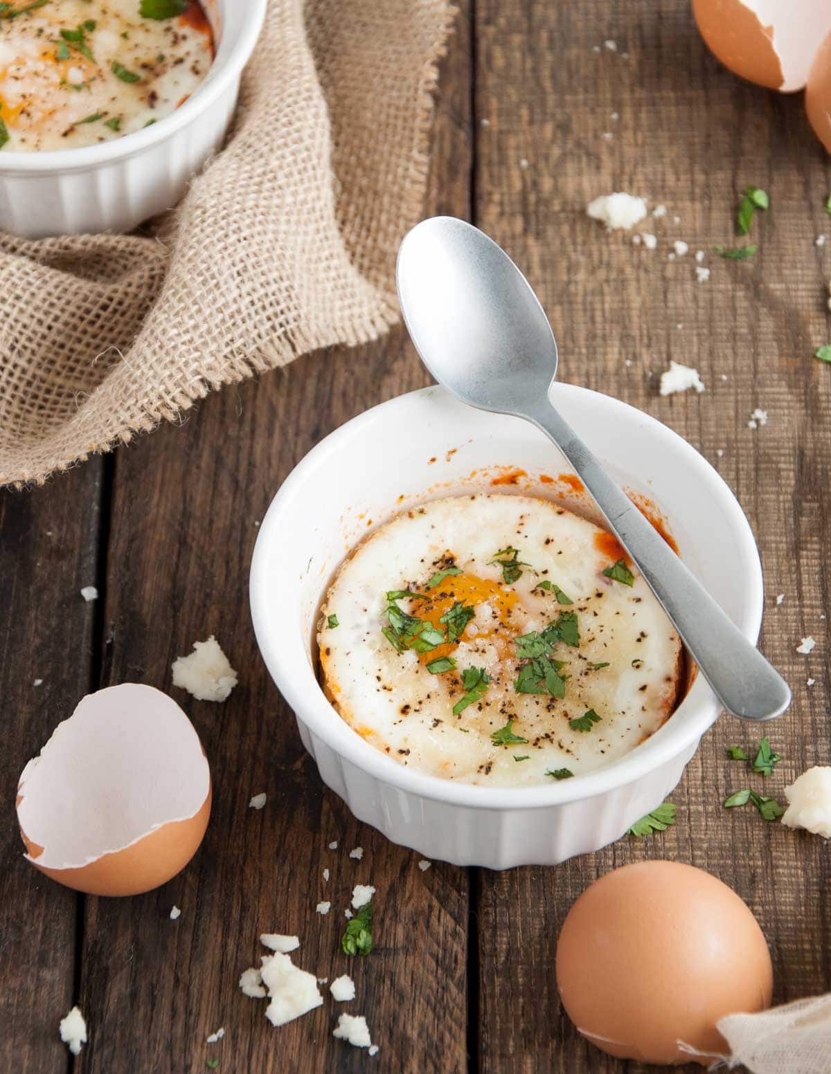 Close up of an egg baked in a white ramekin with a spoon resting over it.
