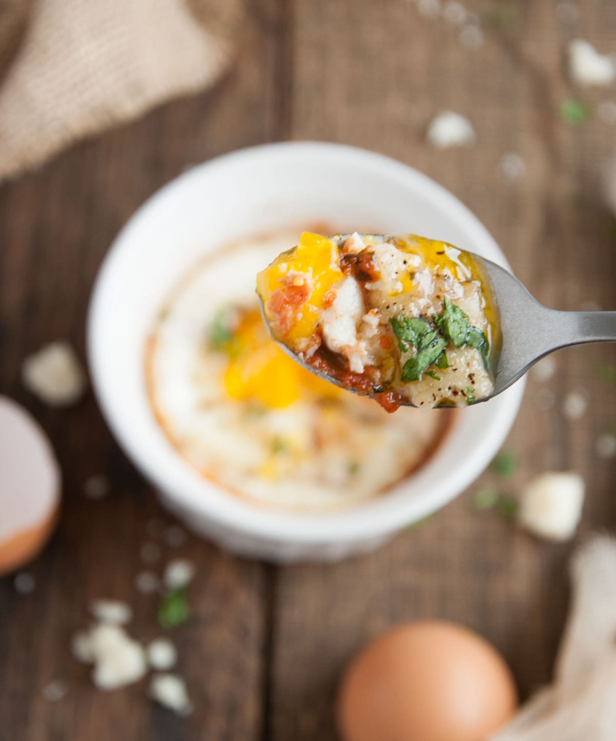 Close up of a spoon with eggs and salsa on it.