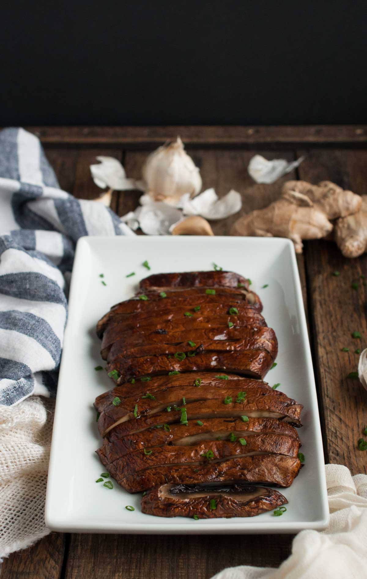 side angle of cooked sliced portobello mushrooms with snipped chives on top and raw garlic and ginger on the side