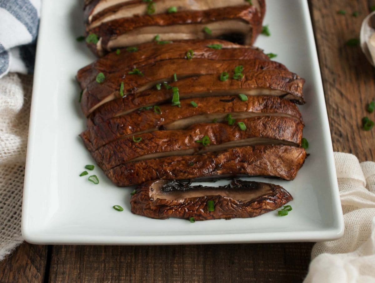 close up side angle of baked portobello mushroom caps sliced and sprinkled with chives on a white plate