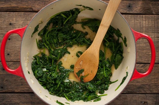 cooked sauteed spinach in a red pot with wooden spoon