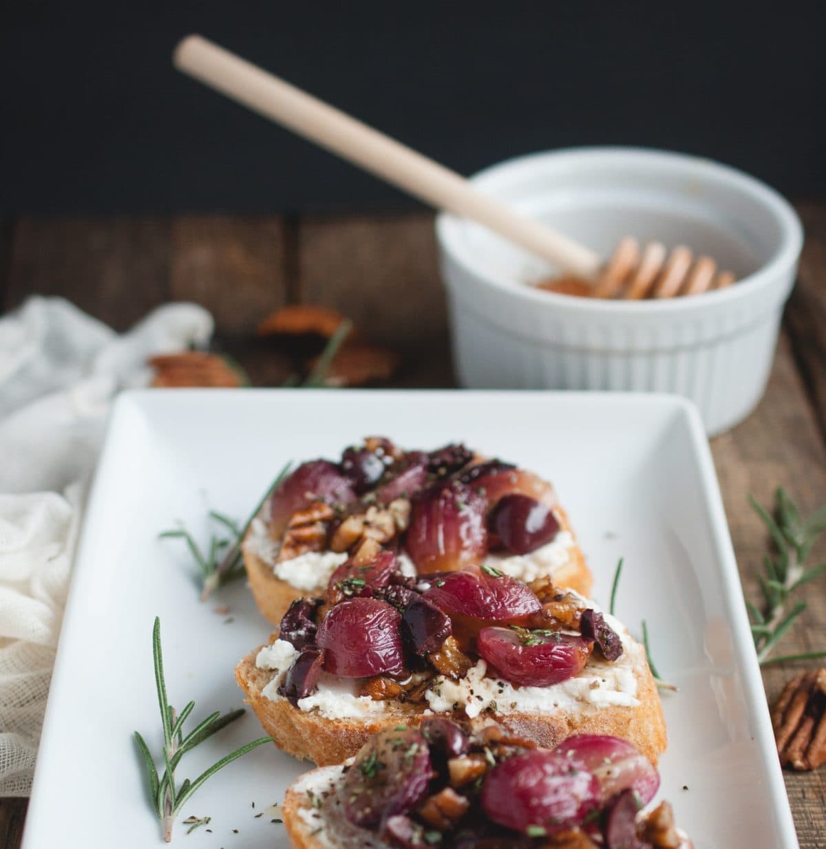 Picture of Crostini with Roasted Grapes on a wood backdrop with rosemary, honey, and pecan garnishes