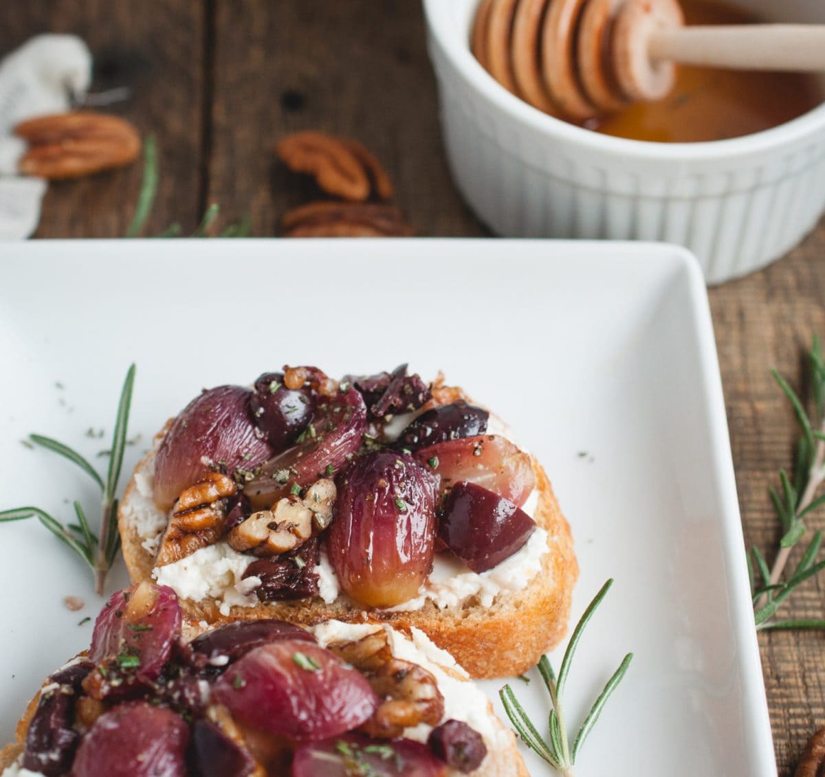 Close up photo of Crostini with Roasted Grapes on a white plate with honey in background