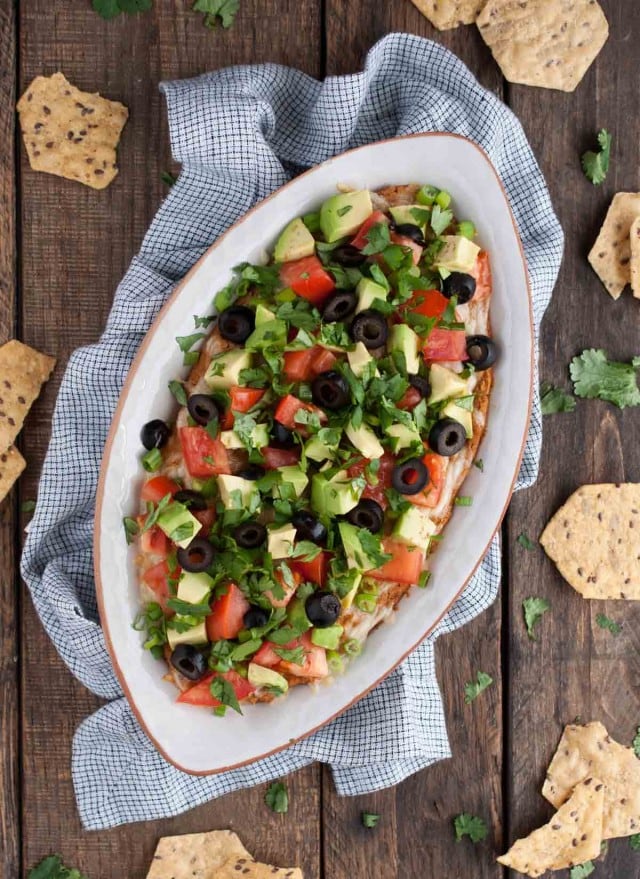 This Mexican bean dip is easy and tasty as can be with Greek yogurt adding a nutrition and protein punch. The melted cheese and toppings take it over the top!