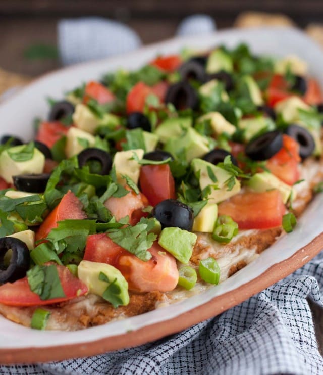 This Mexican bean dip is easy and tasty as can be with Greek yogurt adding a nutrition and protein punch. The melted cheese and toppings take it over the top!