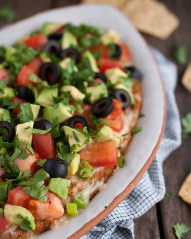 This Mexican bean dip is easy and tasty as can be with Greek yogurt adding a nutrition and protein punch. The melted cheese and toppings take it over the top!