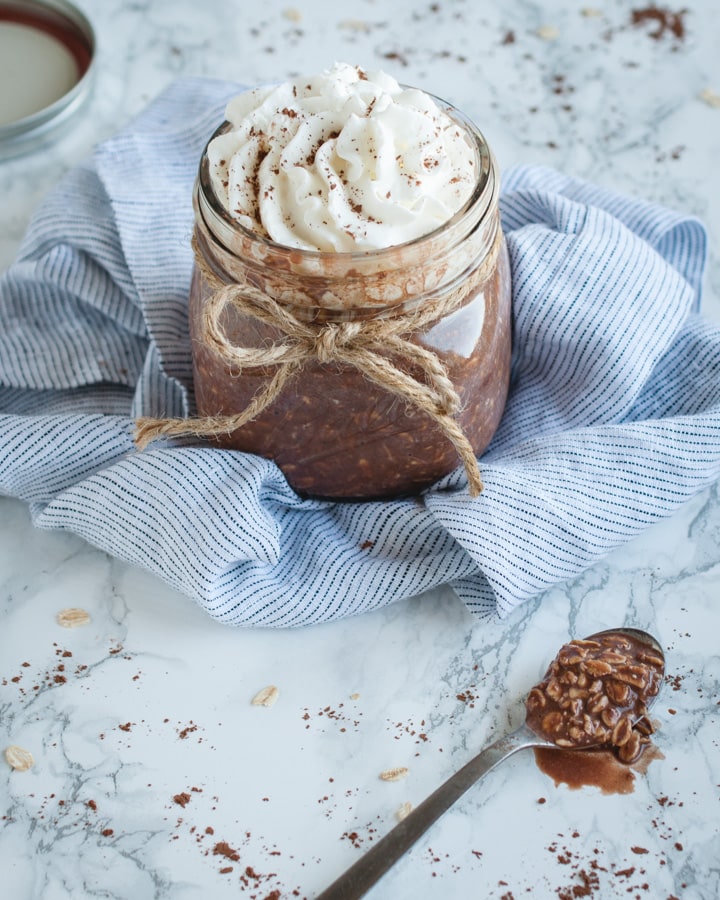 jar of chocolate overnight oats on white background with spoon of oats on it