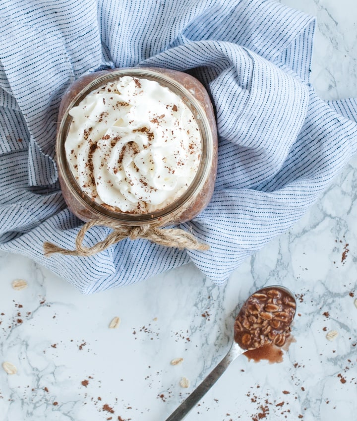 overhead picture of jar with chocolate oatmeal topped with whipped cream and spoonful of chocolate oats next to it