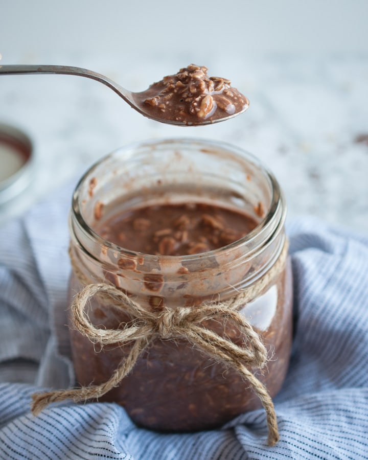 spoon with chocolate oats over jar of chocolate overnight oats