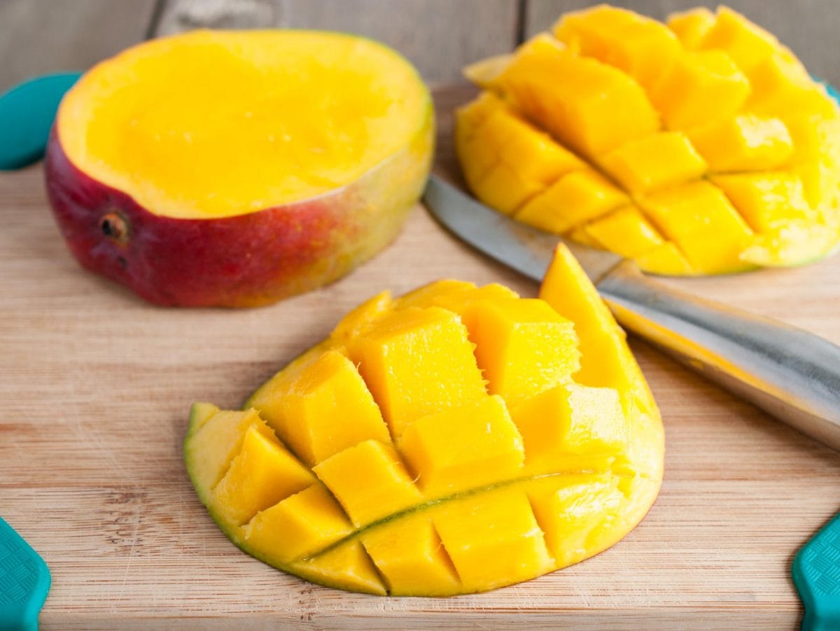 sliced mango still attached to the skin on a wooden cutting board