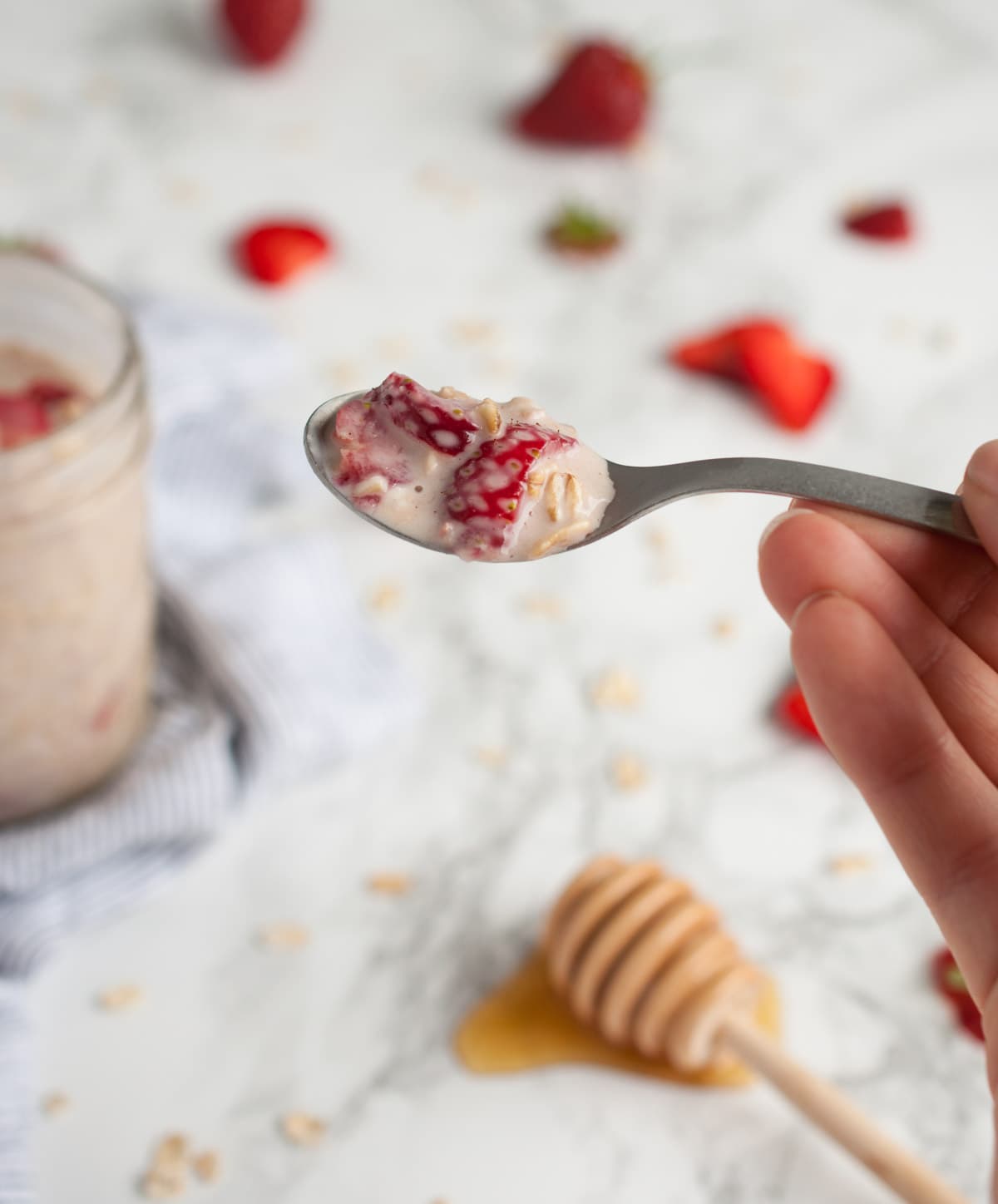 hand holding up a spoonful of strawberry oats with more sliced strawberries blurry in background