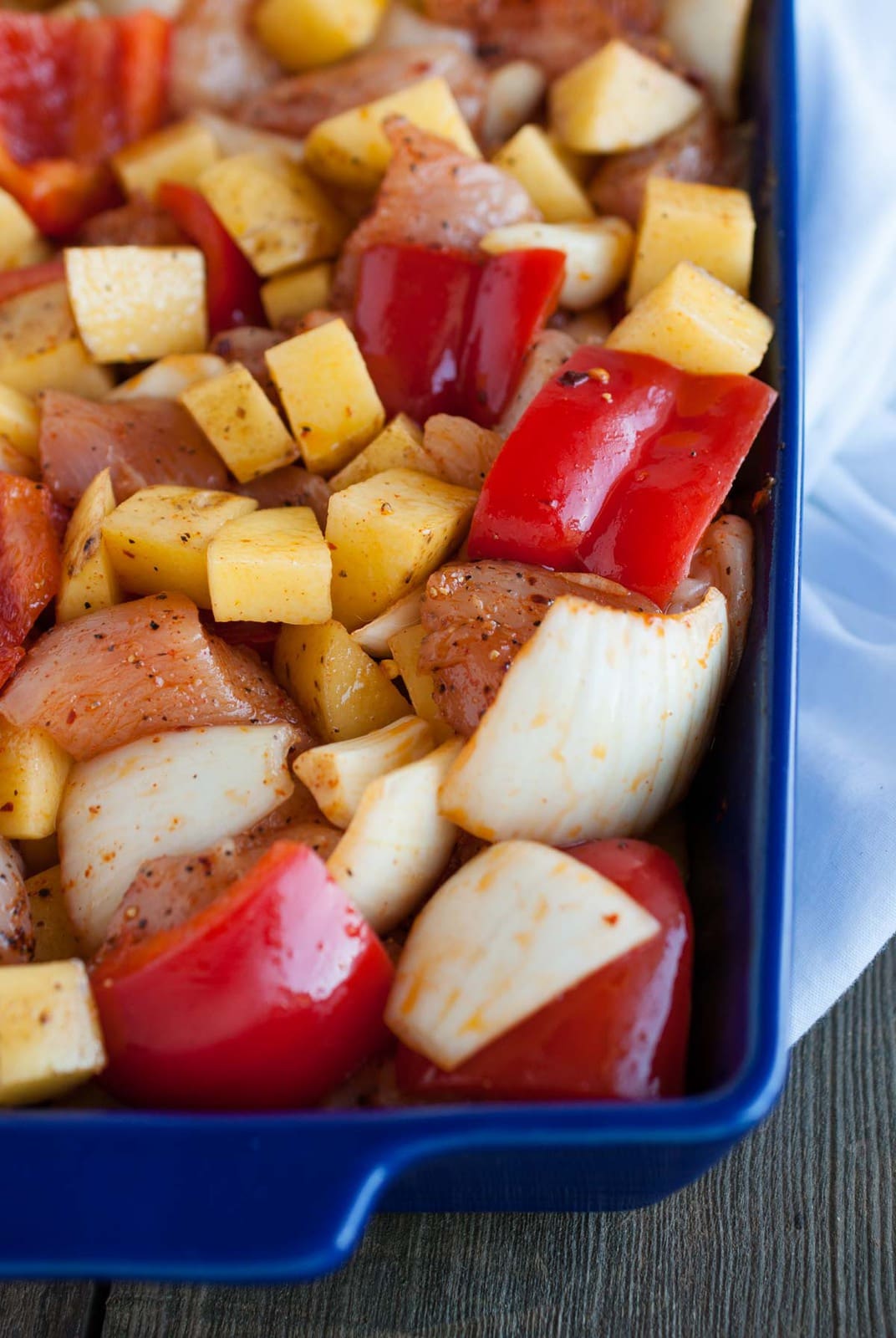 Dish with raw chicken, potatoes, red pepper and onions tossed in spices before baking