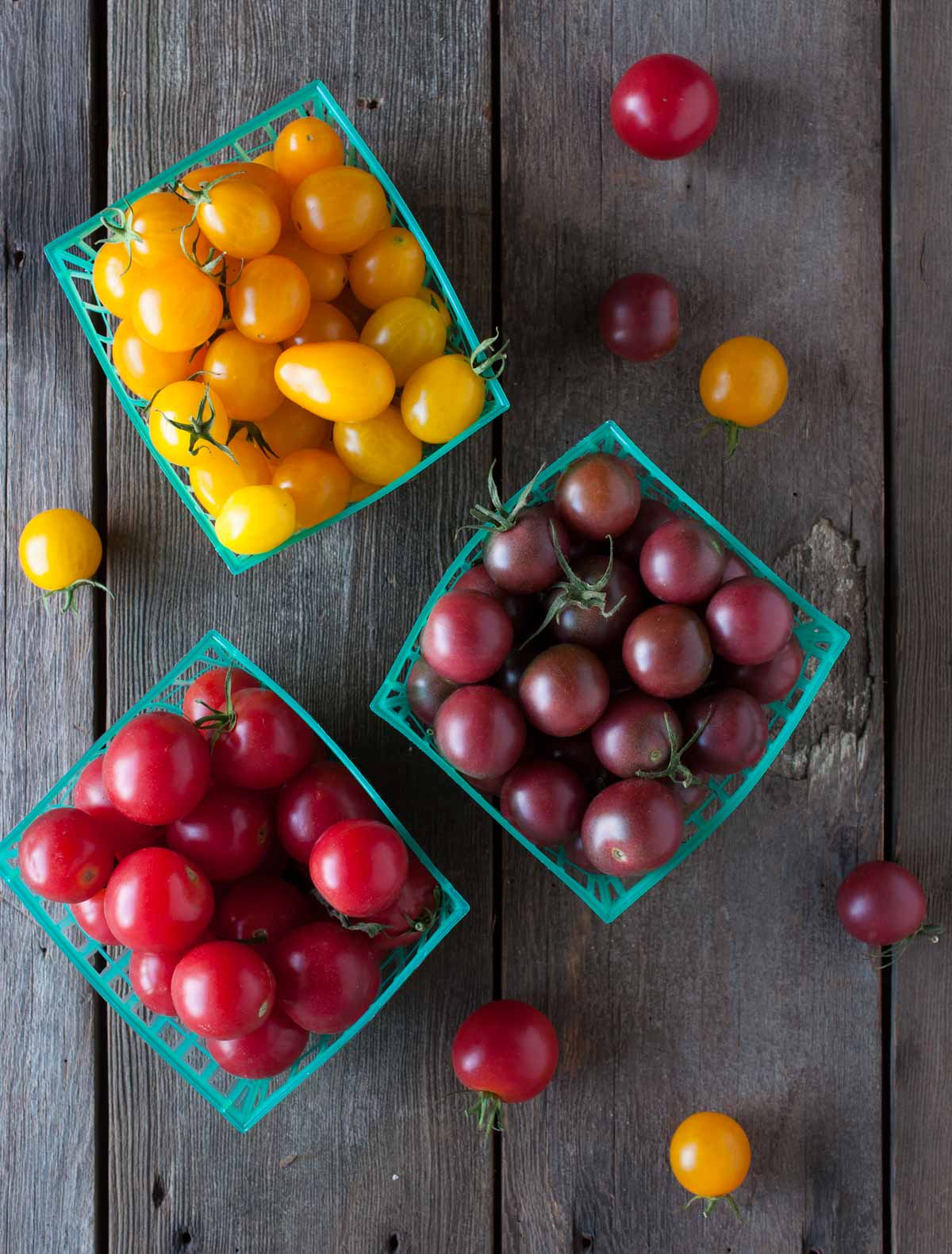 red, yellow and purple cherry tomatoes in blue containers on a wood background