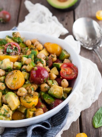 close up of salad with chickpeas and tomatoes on a wood backdrop with ingredients sprinkled around it