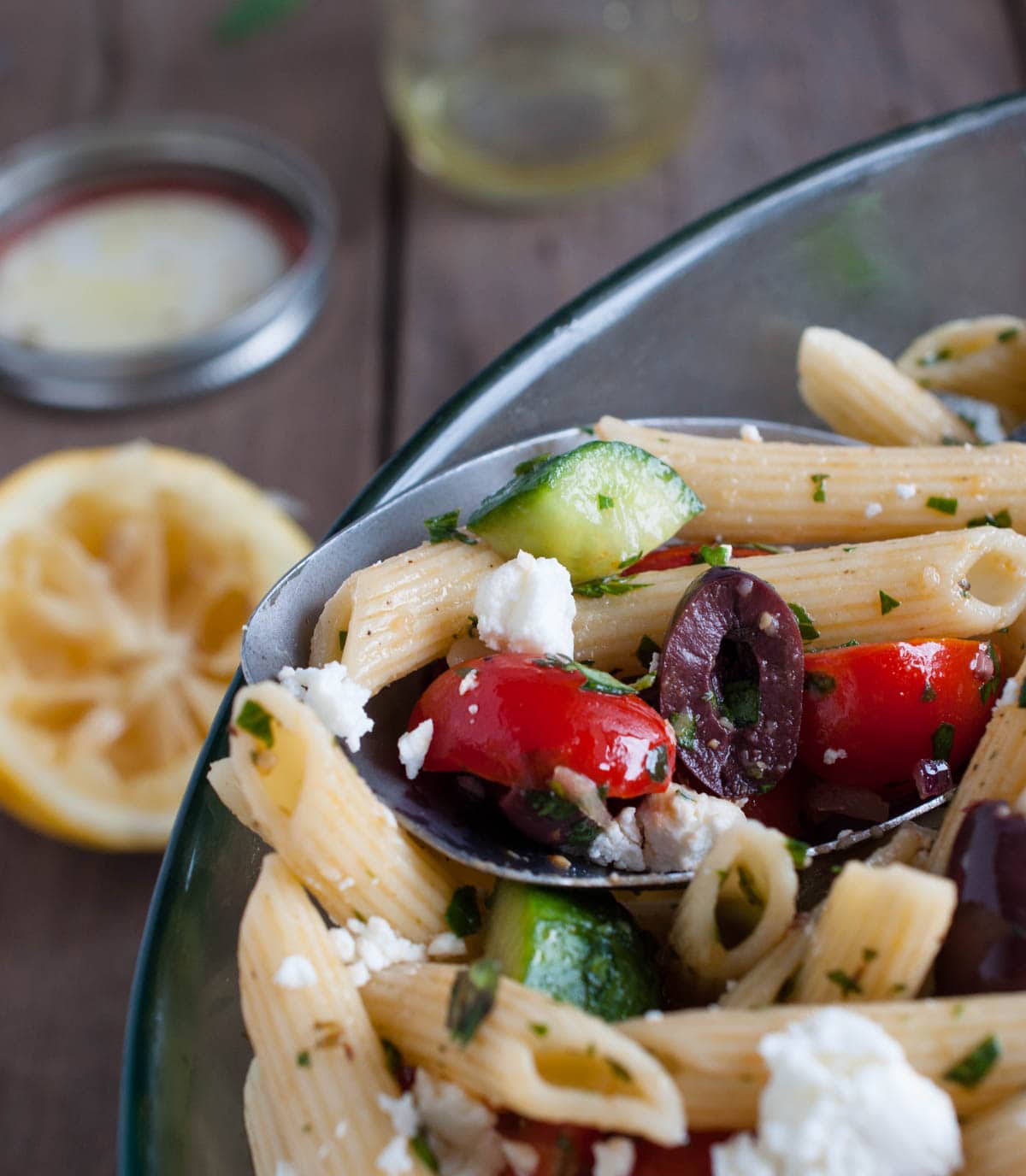 close up of bowl of pasta salad with kalamata olives, cherry tomatoes, cucumber and feta o