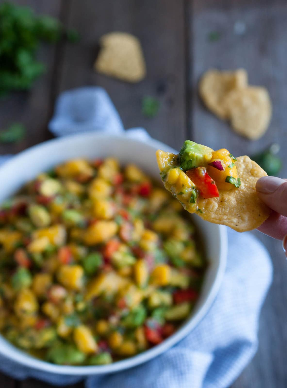 hand holding up chip with mango avocado salsa on it and bowl of salsa in background
