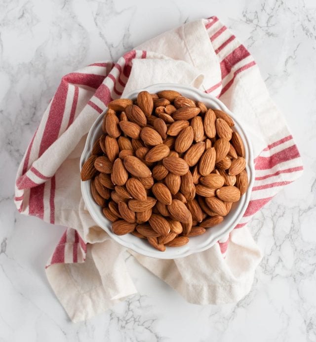 Bowl of raw almonds on marble backdrop