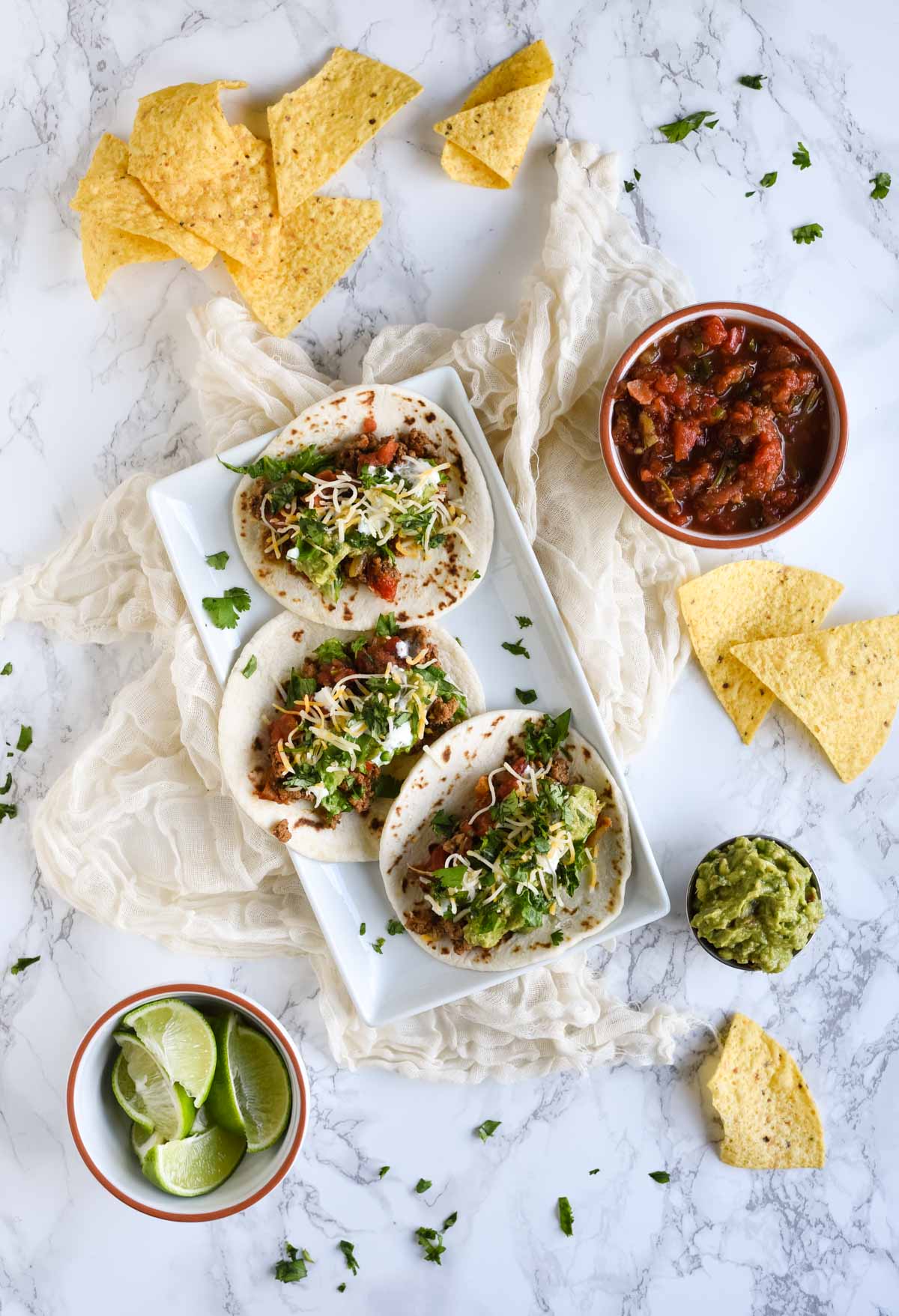 overhead picture of three tacos, chips, and salsa on white background