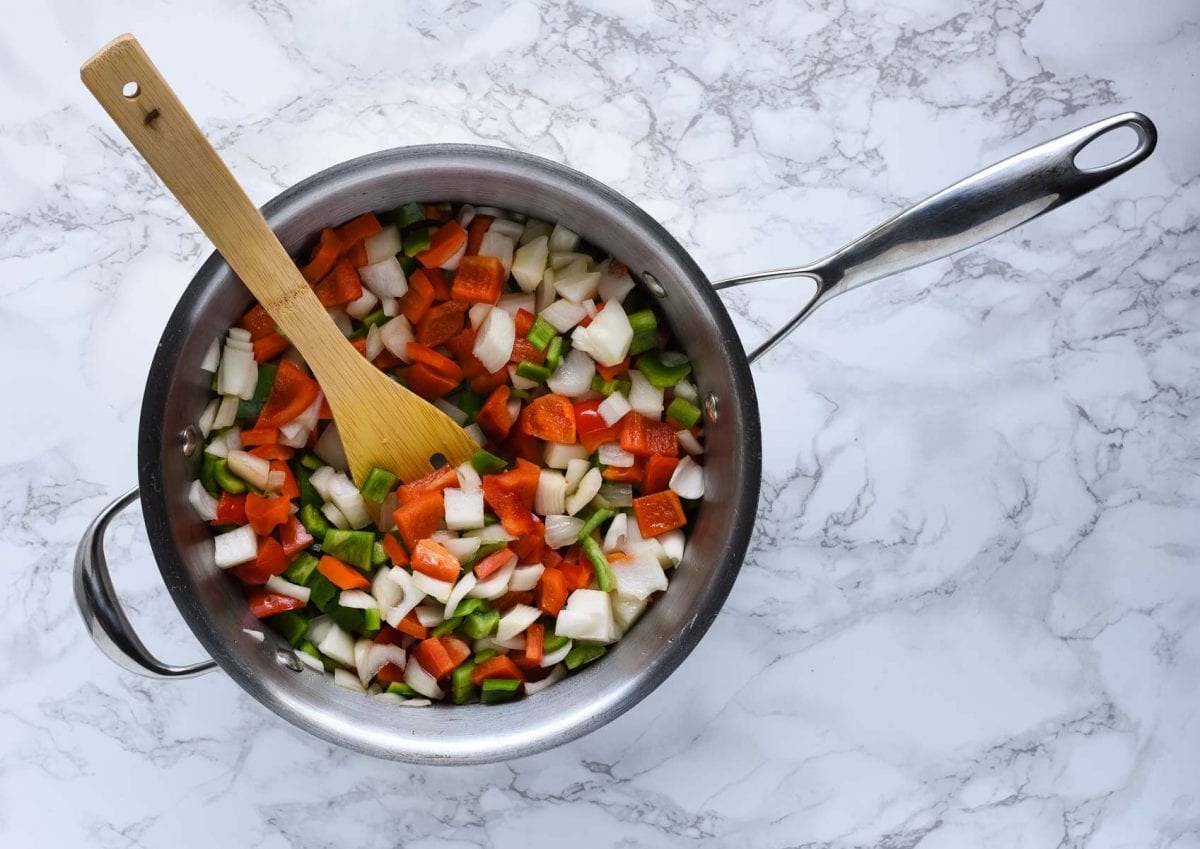 chopped green pepper, red pepper, and onion in a pan with a wooden spoon