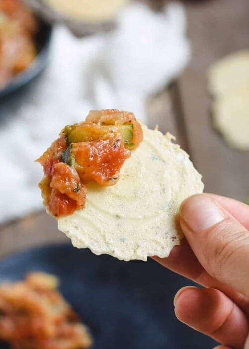 close up picture of hand holding zucchini tomato dip on a cracker