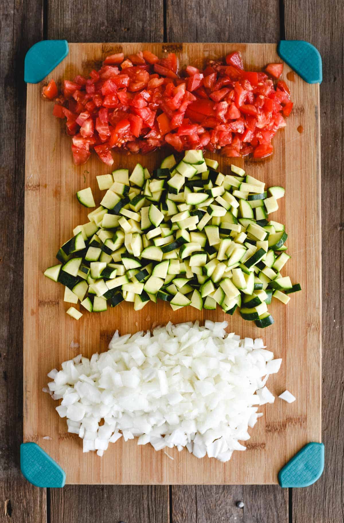 cutting board with zucchini, tomato, and onion chopped on it