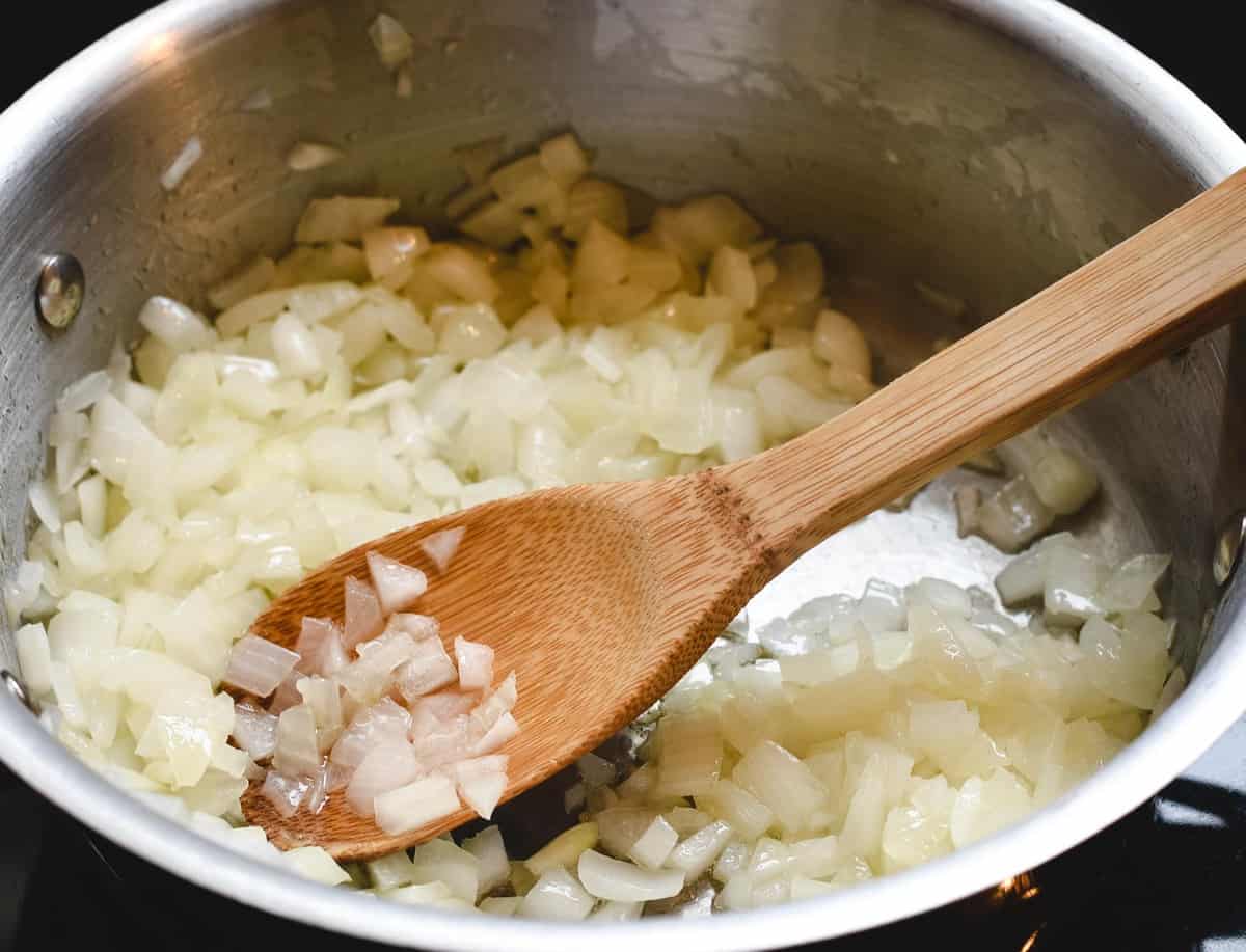 pan with sauteed onion being cooked down and a wooden spoon