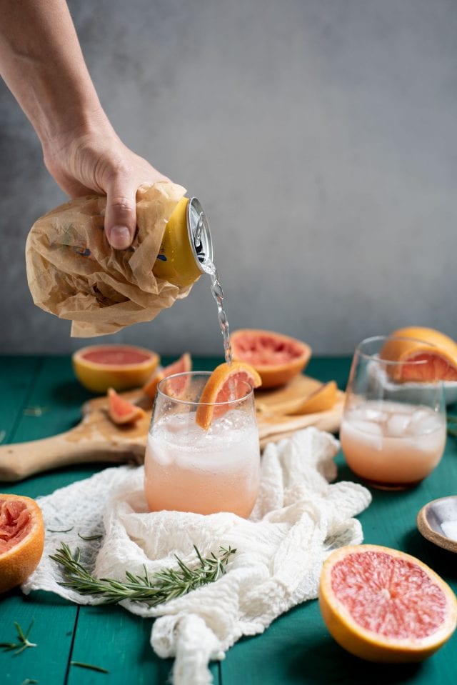 Pouring seltzer water into Rosemary grapefruit mocktail