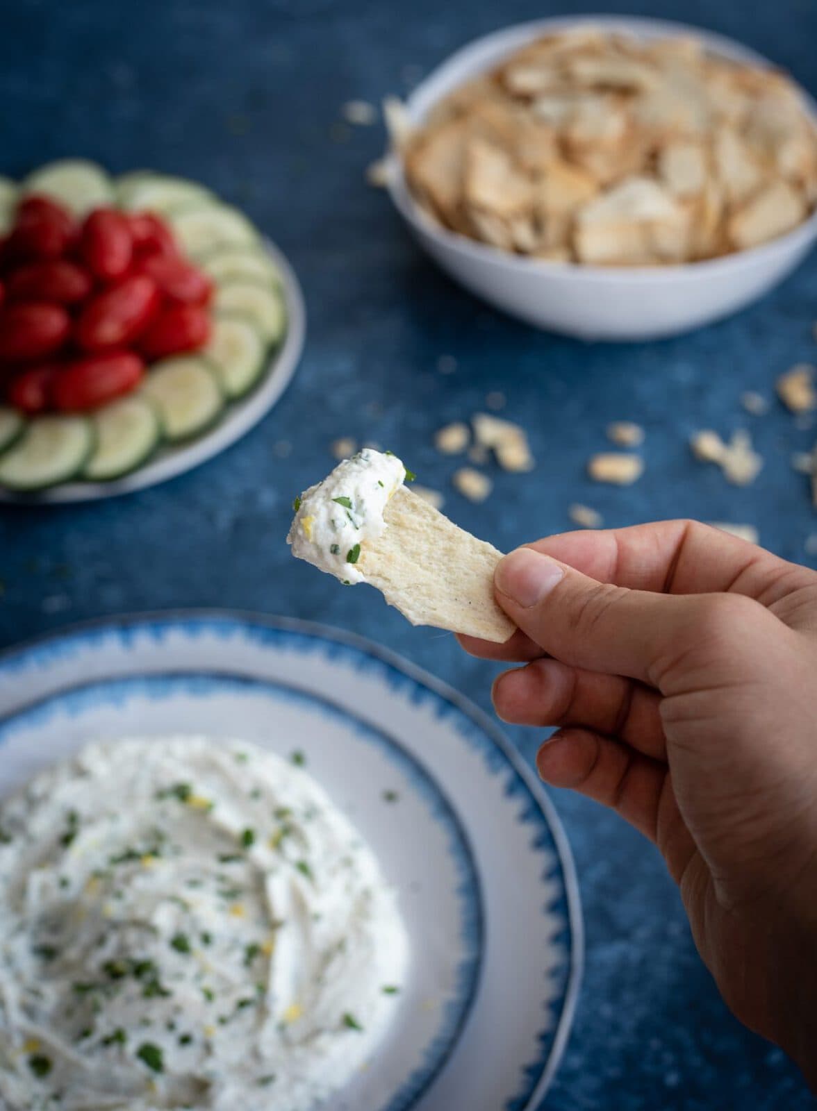 Hand holding cracker with whipped feta and herbs