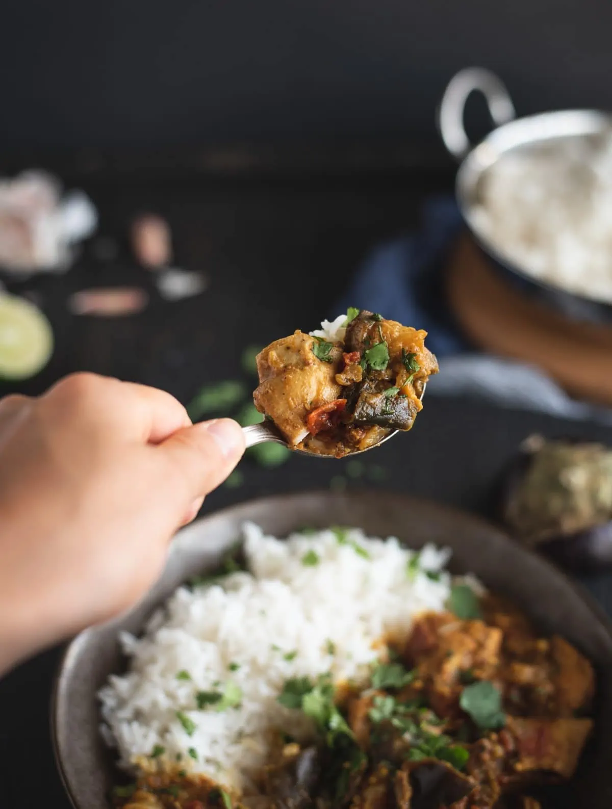 Hand with spoonful of Instant Pot chicken curry with eggplant
