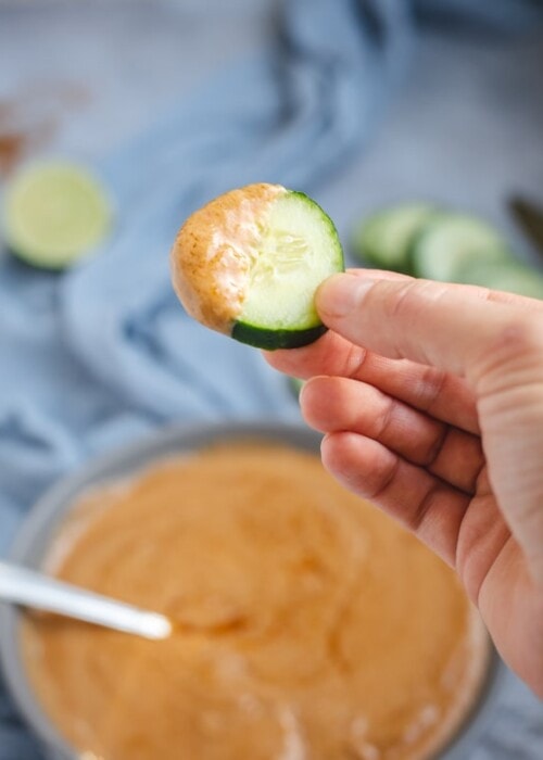 Hand holding cucumber slice dipped in peanut sauce