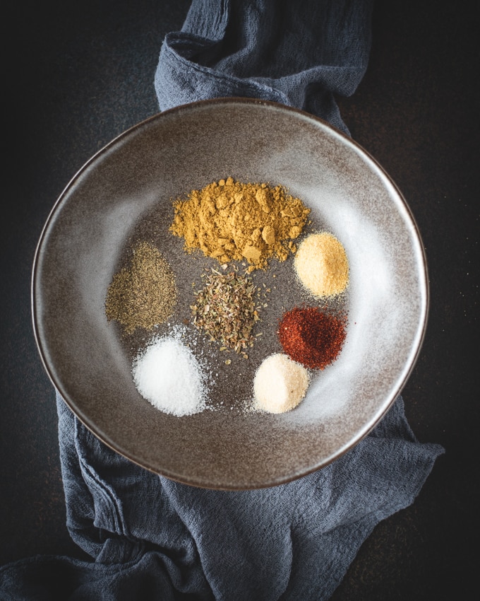 Seven spices on a gray bowl on a black background 