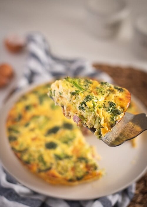 slice of ham and broccoli quiche held up on serving utensil
