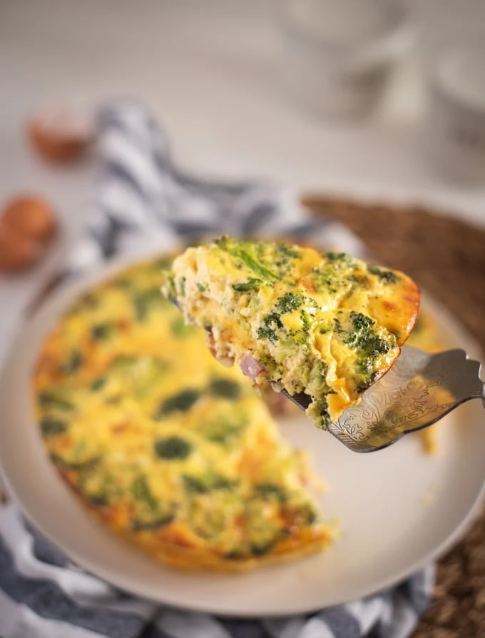 slice of ham and broccoli quiche held up on serving utensil 