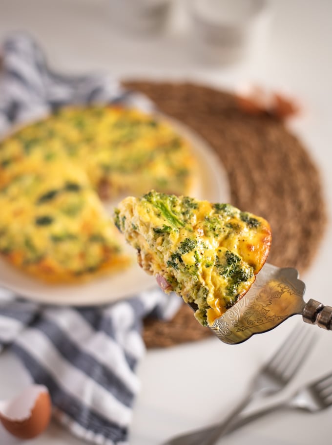 slice of ham and broccoli quiche with rest of quiche in background