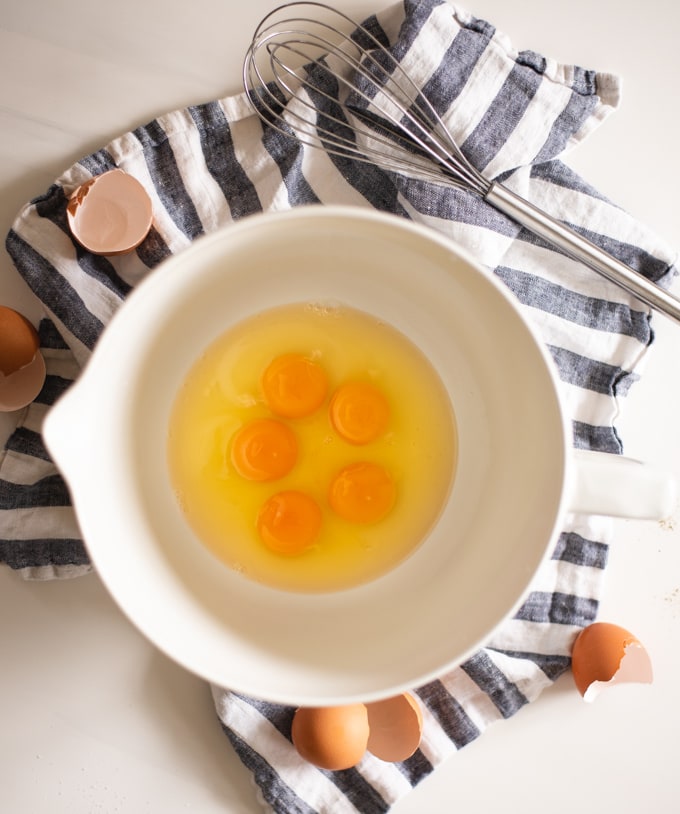 bowl of cracked eggs on a blue and white kitchen towel