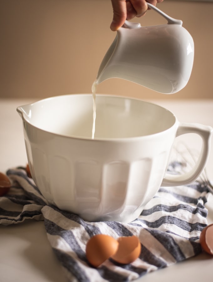 White pitcher pouring milk into a white mixing bowl