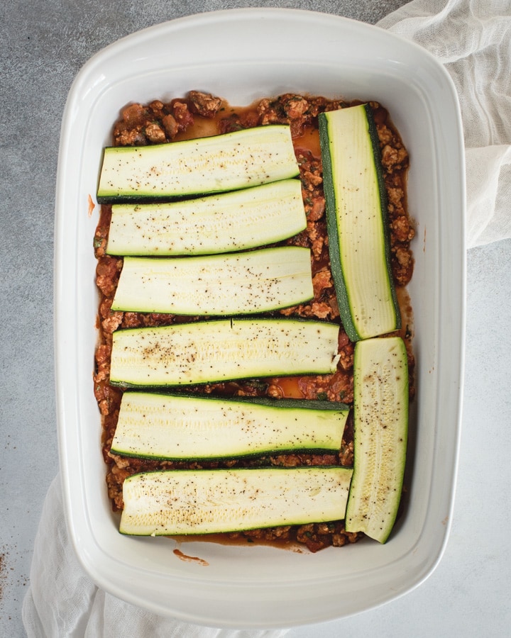 baking dish with red sauce and zucchini slices