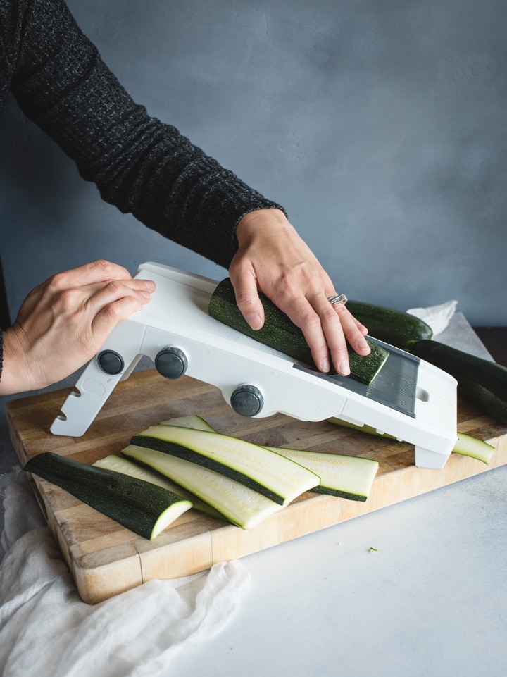 zucchini being sliced on mandolin slicer