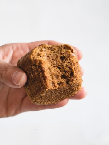 Close up picture of hand holding pumpkin muffin against white background