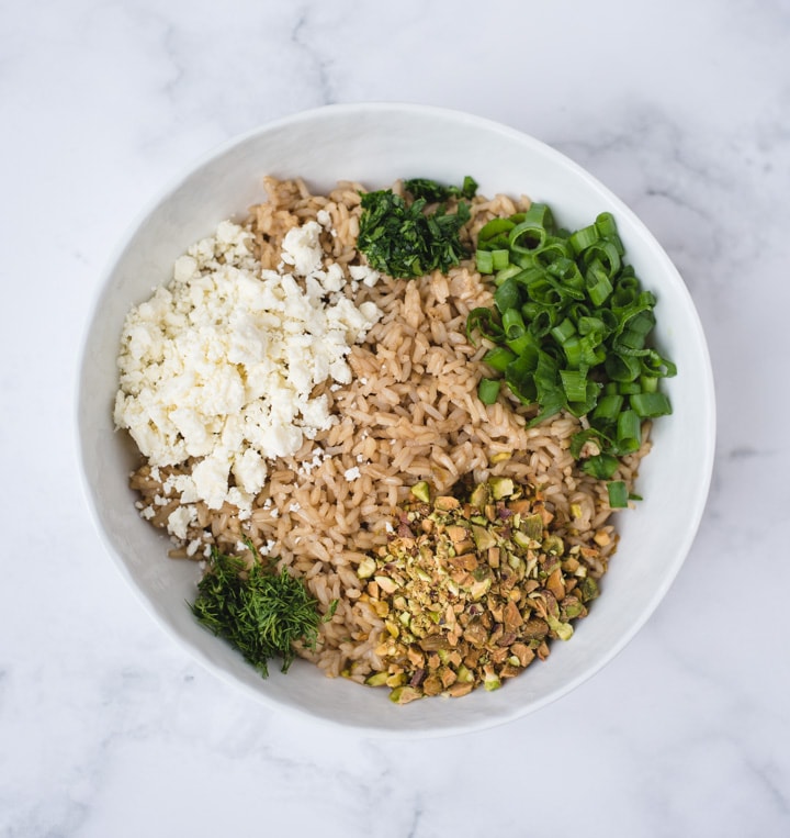 Bowl with brown rice, herbs, pistachios and feta on white background