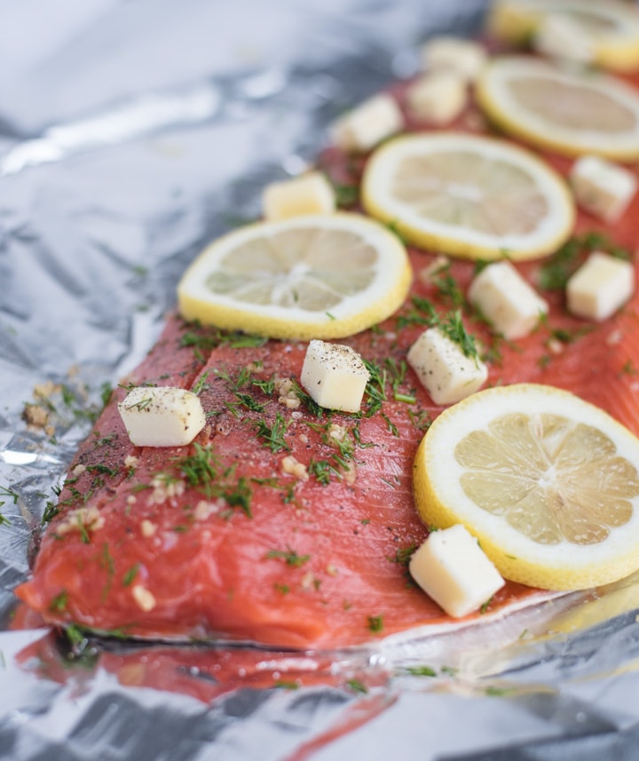 Raw salmon filet topped with butter, lemon, and dill on foil 